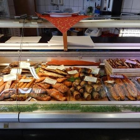 Verkaufstheke mit Räucherfisch und Fischspezialitäten. Eine gekühlte Verkaufstheke mit verschiedenen Fischprodukten wie Rollmops, Lachsfilets und geräucherten Fischen. Die Ware ist mit kleinen Schildern beschriftet.