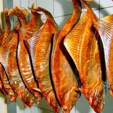 Geräucherte Schollen an Haken. Mehrere goldbraun geräucherte Schollen hängen nebeneinander an Haken in einem gekachelten Raum.