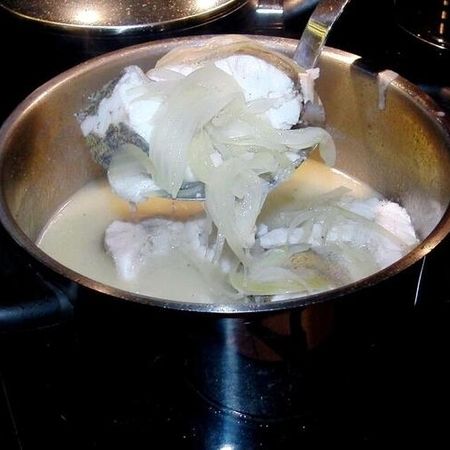 Gekochter Fisch mit Zwiebeln in einer Brühe im Kochtopf. Fischstücke mit Zwiebeln werden in einem Topf in heller Brühe gegart und mit einer Schöpfkelle entnommen.