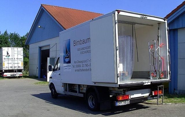 Lieferwagen von Birnbaum & Kruse vor einem Firmengebäude. Die geöffnete Ladefläche zeigt eine isolierte Kühlkammer mit Vorhang und Rollwagen.