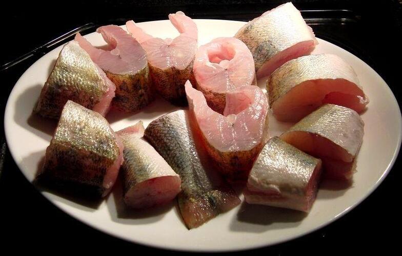 Roh vorbereiteter Fisch auf einem weißen Teller angerichtet. Mehrere rohe Fischstücke mit Haut liegen auf einem weißen Teller, bereit zur weiteren Zubereitung.